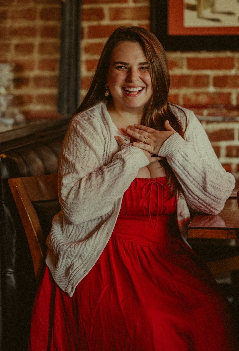 Andrea laughing with her hands on her chest, wearing a cream cardigan