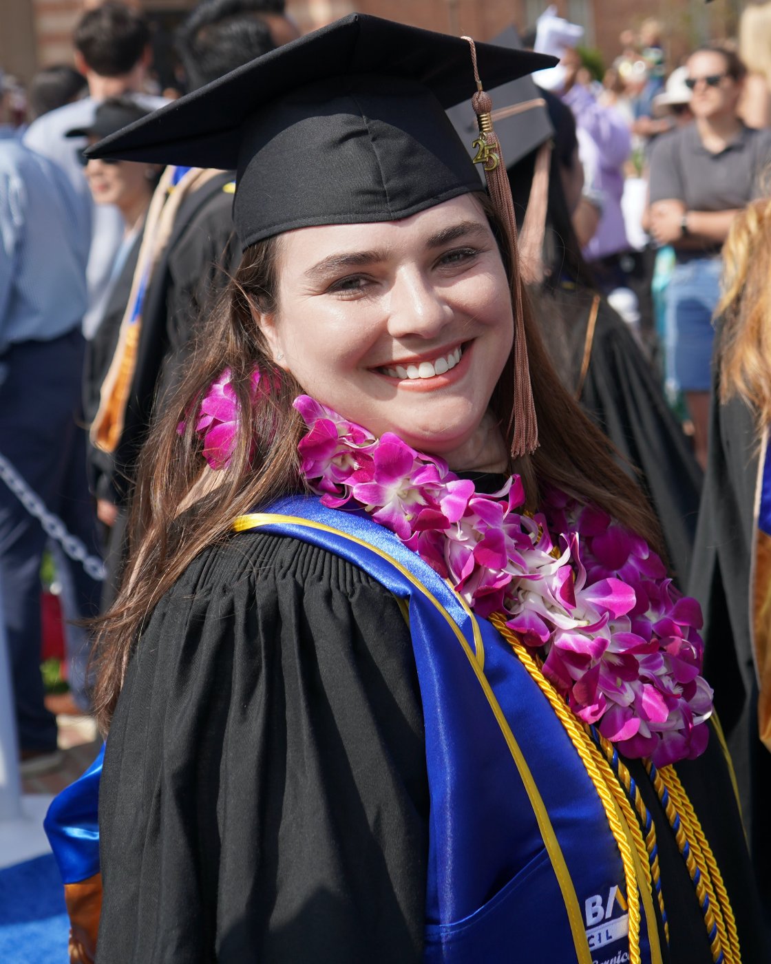 Andrea smiling in her graduation cap and gown with an orchid lei at UCLA commencement