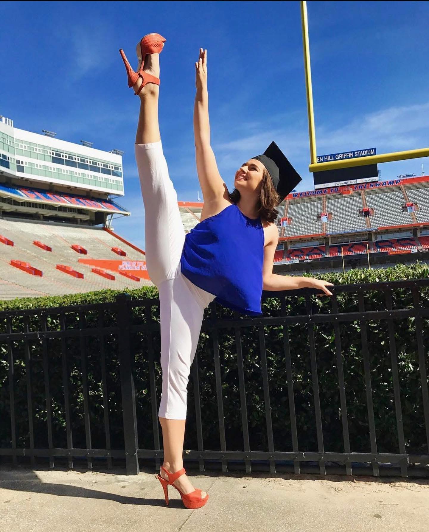 Andrea in a high dance kick at her University of Florida graduation, wearing a cap